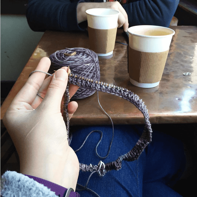 Holding a newly-casted-on knitting project, a hat with purple yarn.